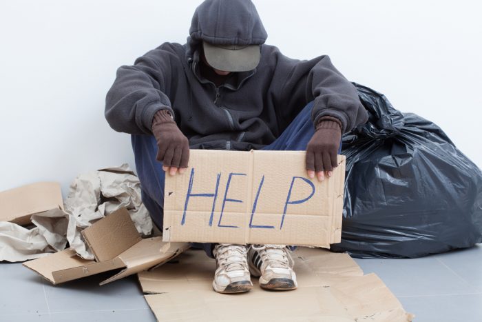 A homeless African American man holds up a cardboard sign that reads, "Help."